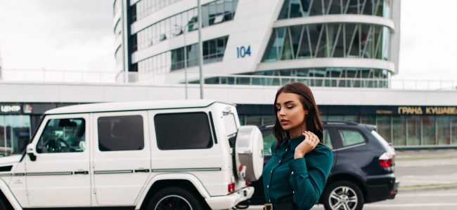 Stylish beautiful girl in dress walking in street. Full length stock photo of a pretty brunette woman in long emerald green dress with buttons and black leather heels walking confidently along the street against modern buildings and cars.