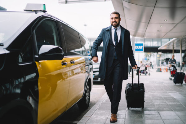 Cheerful man with luggage getting in taxi near airport Cheerful man with luggage getting in taxi near airport